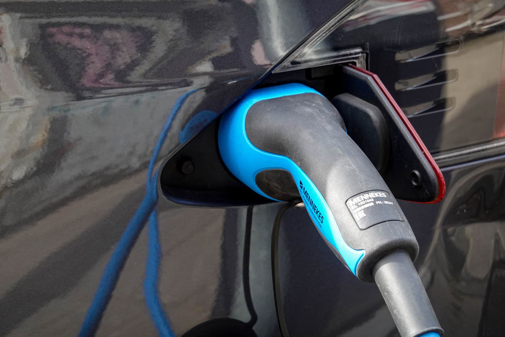 An EV charging connector held next to a car's charge port